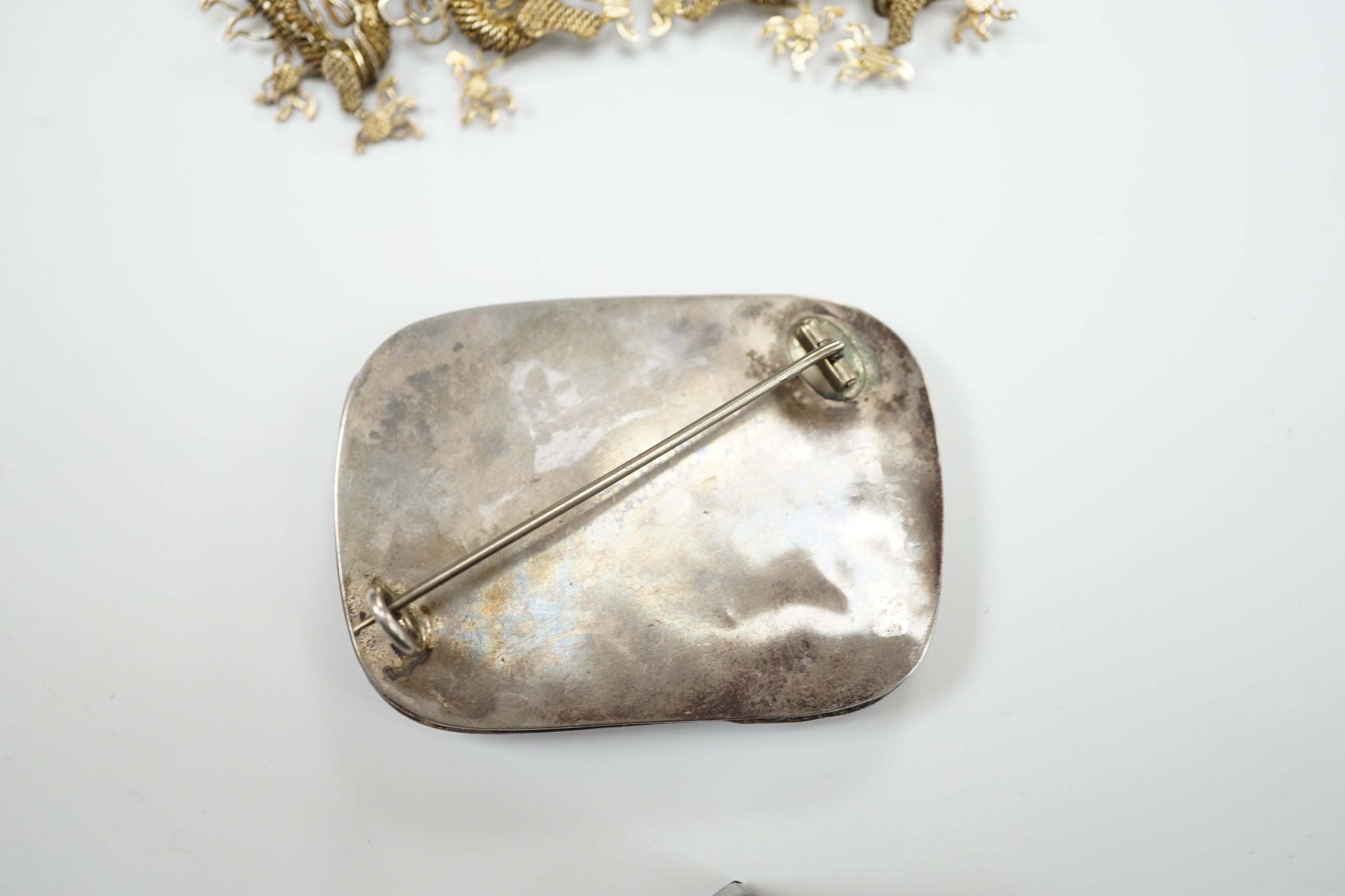A Chinese? white metal and polychrome enamelled brooch, depicting a hare amongst foliage, 59mm(a.f.), together with a similar gilt white metal filigree and cabochon green paste set brooch.